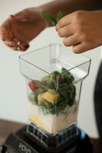Hands adding mint to a clear VOID jar filled with greens, fruit and liquid