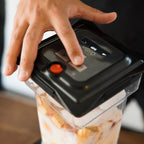A hand pressing the button on the VOID vacuum lid, seated on a jar of cut fruit