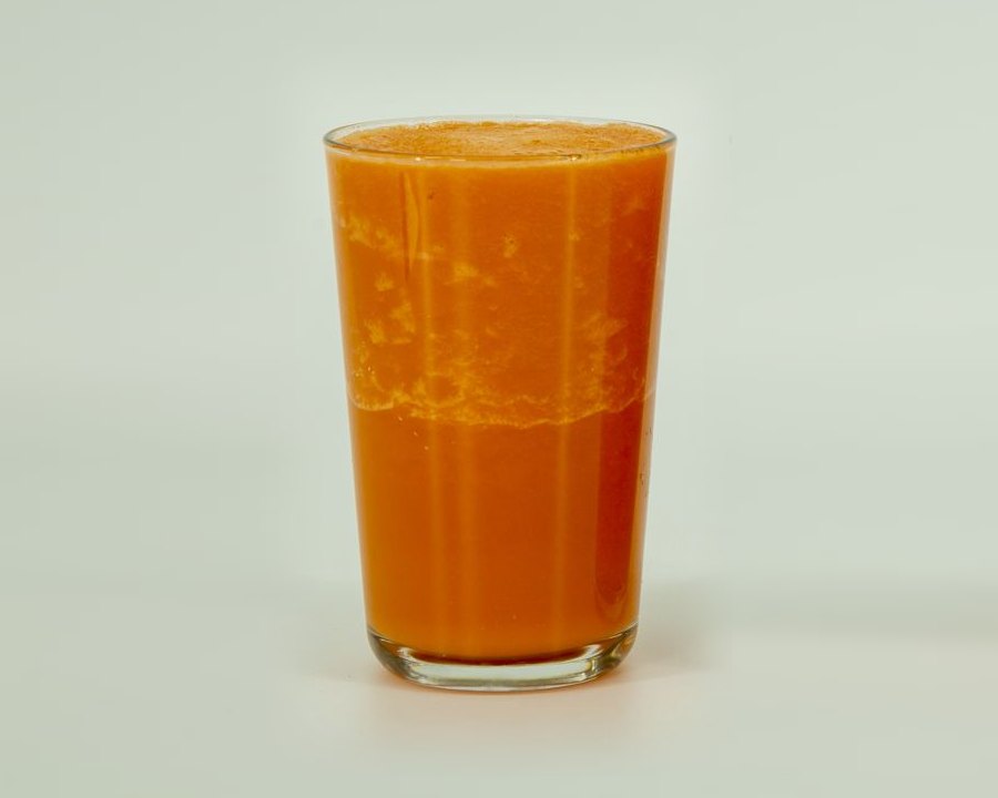 Carrot smoothie blended with the vacuum off, photographed 20 minutes after pouring. A pale, mottled layer has risen over darker liquid, with a visible separation line partway down the glass.