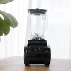 The VOID Complete System blender on a wooden counter with its basic lid on, a plant and a curtain behind it